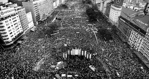 Vista aérea de multitudinario acto en la Plaza de Mayo y Avenida 9 de Julio, Buenos Aires, en los albores del retorno a la democracia en Argentina, 1983. Miles de personas reunidas celebrando la recuperación de las instituciones y la libertad.