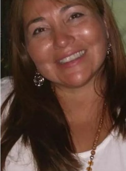 Retrato de la doctora Elena Zemma, médica neurocirujana pediátrica, sonriente, con cabello castaño largo y accesorios dorados, sobre fondo neutro.
